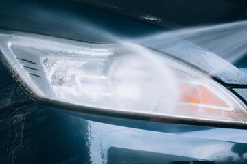 Car wash. Selective focus headlight close-up while washing with water and foam. A stream of water...