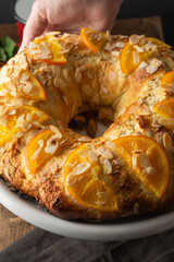 Close-up of Kings cake with pieces of orange and almonds, freshly made on white plate, on dark background, in vertical
