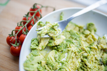 Cherry tomatoes and bowl of mashed avocado on wooden table