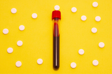 Laboratory test tube with blood is on yellow background surrounded by white tablets making up the ornament in polka dots. Concept art photo for use in medicine, hematology, diagnosis of blood diseases