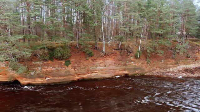 Red sandstone cliffs in the banks of river Salaca during late autumn time, Latvia. Real time drone footage
