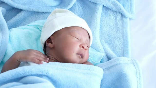 A cute little african newborn baby is relaxing, lying on bed. Close-up portrait of a playful and energetic child.