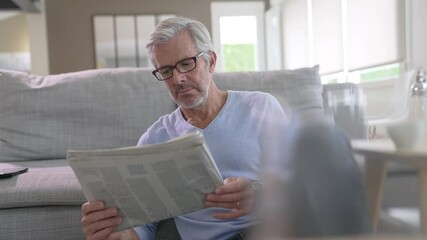 Attractive senior man with eyeglasses relaxing at home reading newspaper - Powered by Adobe