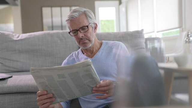 Attractive senior man with eyeglasses relaxing at home reading newspaper