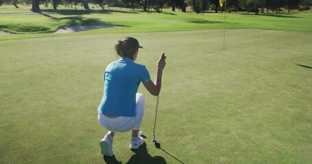 Caucasian female golf player reaching for a ball standing on golf field