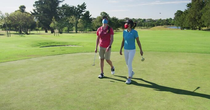 Two caucasian women playing golf wearing face masks walking together