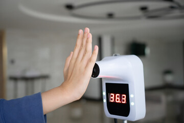 raising hand close to digital Infrared thermometer   for check temperature measurement screening from COVID-19 for check in building ,hotel ,restaurant or lobby , in soft focus