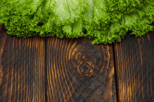 Green lettuce leaves on brown wooden overlaid background with empty space for text, template design concept, food advertising, healthy food, spring and summer vitamins, food preparation ingredients