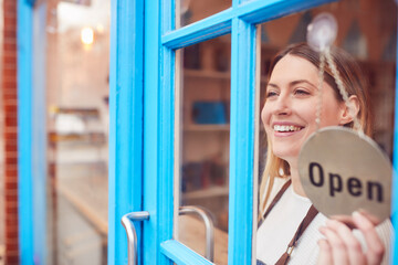 Female Small Business Owner Turning Around Open Sign On Shop Or Store Door