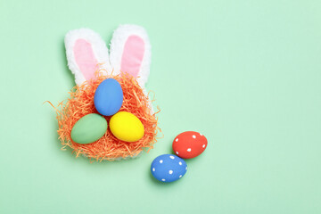 Easter eggs in a nest, bunny ears on a mint green background. Greeting card with copy space flat lay.