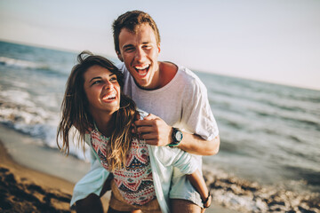 Young woman giving piggyback ride to boyfriend on beach.
