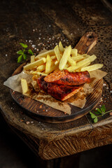 Grill house concept. Grilled, roasted tasty sausage with french fries on the old wooden cutting board.