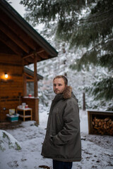 Handsome man standing with a cabin and snowy pines as background