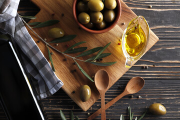 Composition of green olives, olive oil, spices, marinade on a wooden background with space for text.