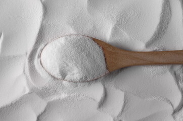 Baking soda pile, sodium bicarbonate with wooden spoon, background and texture