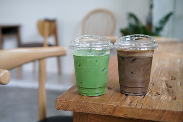 Iced Matcha and Hojicha. Two plastic cup of matcha green tea drinks, green and dark brown colour on wooden table.