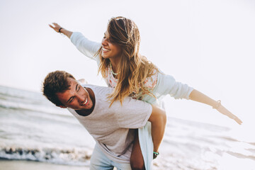 Young man giving piggyback ride to girlfriend on beach.