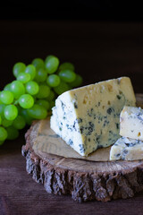 
blue cheese on a wooden frame on a wooden background with white grapes in rustic style