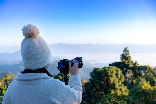 Rear tourist woman taking photo with digital camera at top mountain in the winter northern Thailand