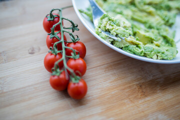 Cherry tomatoes and bowl of mashed avocado on wooden table