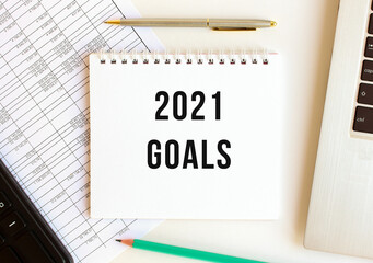 Notepad with text 2021 GOALS on a white background, near laptop, calculator.