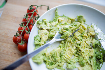 Cherry tomatoes and bowl of mashed avocado on wooden table