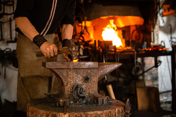 The blacksmith forging the molten metal on anvil in smithy. Blacksmith at the workshop. Working metal with hammer and tools in forge