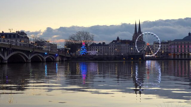 The Ferris wheel, two carousels and the cathedral reflecting on the river Adour at sunset in Bayonne, France