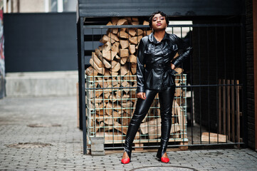Fashionable beautiful african american woman posing in black leather jacket and pants at street.