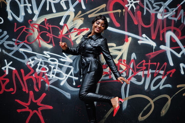 Fashionable beautiful african american woman posing in black leather jacket and pants at street...