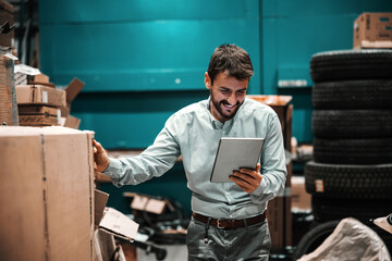 Smiling bearded supervisor looking at tablet and checking on box ready for shipment. Export firm.