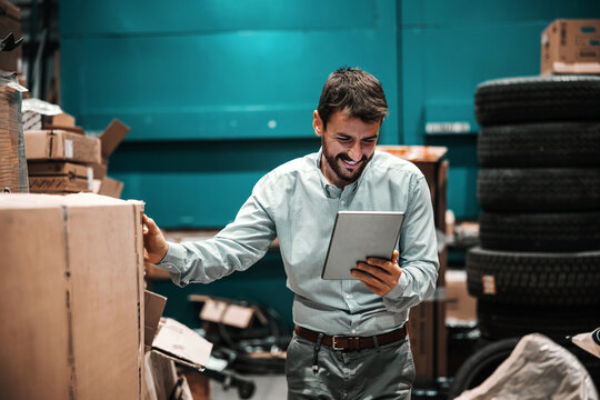 Smiling bearded supervisor looking at tablet and checking on box ready for shipment. Export firm.