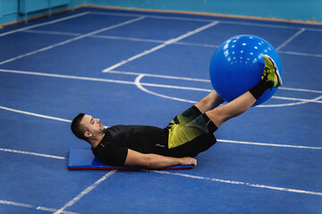 Fit sportsman in excellent shape doing Crunches with pilates ball in sport hall.