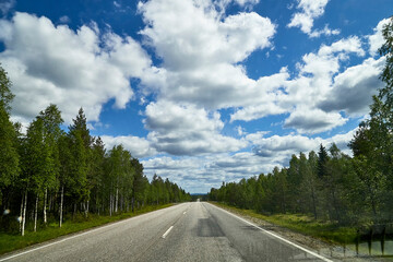 View from relief car windscreen on the blue sky with white clouds, grey asphalt road and landscape with forest and green teeses. Landscape through window