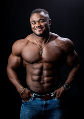 Fototapeta na wymiar African american bodybuilder stands with hands in pockets on black studio background. Strong body.