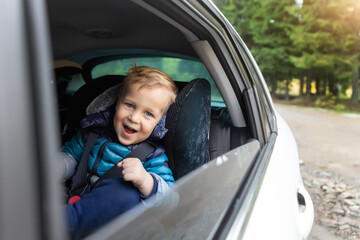 Little cute adorable happy caucasian toddler boy sitting in child safety seat car open window enjoy having fun making road trip nature countryside forest landscape. Family car travel by car concept