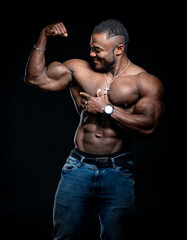 Smiling bodybuilder with strong body poses to the camera with naked torso. Athlete showing strong hands. Black background.
