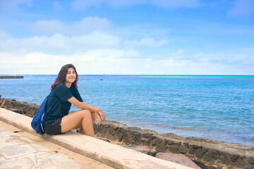 Teen girl sitting on walking path next to blue ocean
