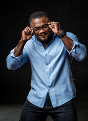 African american manager in stylish light shirt and fashion glasses poses on black background.