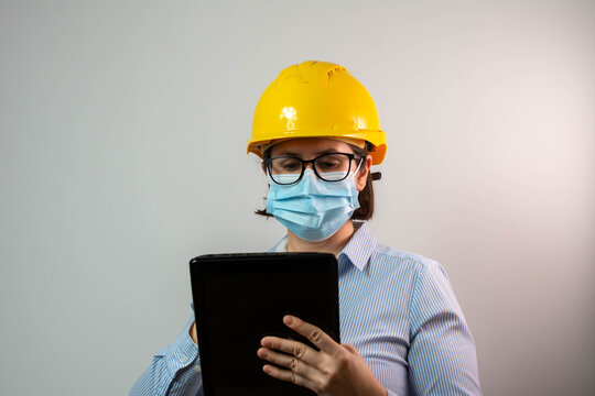 Female engineer using digital tablet while having conference call and wearing protective face mask due to coronavirus pandemic.