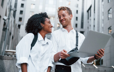 Uses laptop. Man with afrian american woman together in the city outdoors