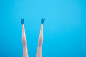 Female doll legs upside down on light blue background