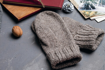 Gray knitted mittens lie on the table next to New Year's cards and books. Self made. Foreground.
