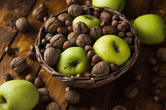 Walnuts With Green Apples Mixed With A Wicker Basket. A Wooden Table On Which Nuts And Apples Are Scattered