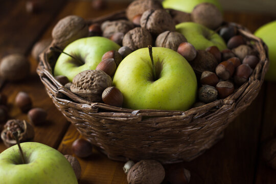 Walnuts With Green Apples Mixed With A Wicker Basket. A Wooden Table On Which Nuts And Apples Are Scattered