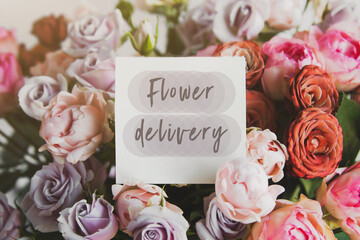 white gift card with the inscription flower delivery in a bouquet of bright beautiful multi-colored roses, the concept of delivery service