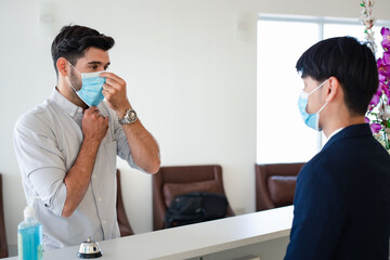 Obraz premium Check in hotel. Vistor and receptionist at counter in hotel wearing medical masks