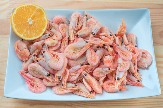 Prepared small shrimps on a white plate over wooden table with lemon. top view