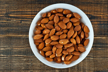 Almonds in a white bowl on an old shabby board. Nuts on a brown wooden table.