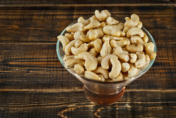 Cashews in a clear glass bowl on an old shabby board. Nuts on a brown wooden table.